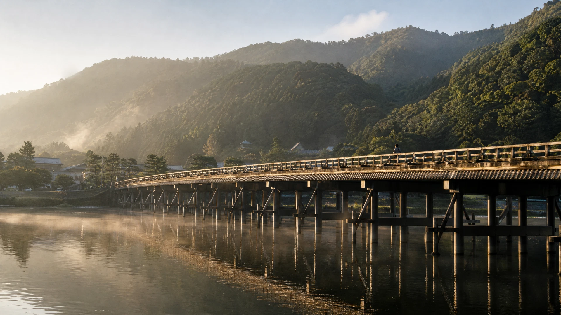 Arashiyama’s riverside at sunrise with Togetsukyo Bridge, misty hills, and an early pedestrian.
