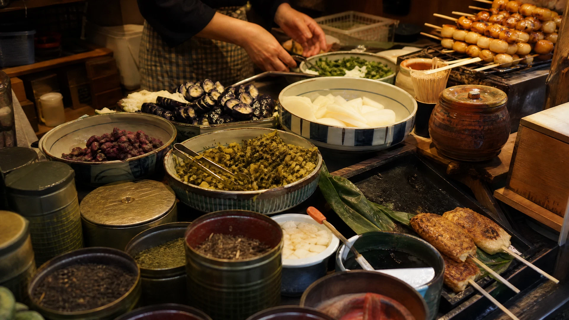 A vendor’s counter at Nishiki Market with carefully arranged pickles, tea tins, and warm grilled snacks.